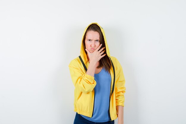 Young lady holding hand on chin in t-shirt, jacket and looking gloomy