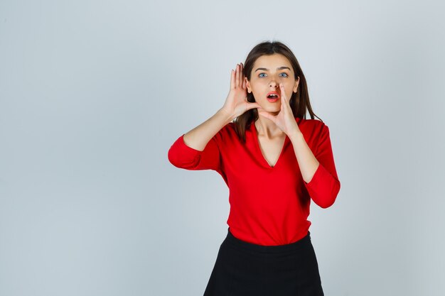 Young lady holding hand behind ear while telling secret in red blouse