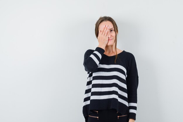 Young lady holding hand on eye in casual shirt and looking optimistic