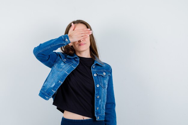 Young lady holding hand on eyes in blouse, jacket and looking positive. front view.