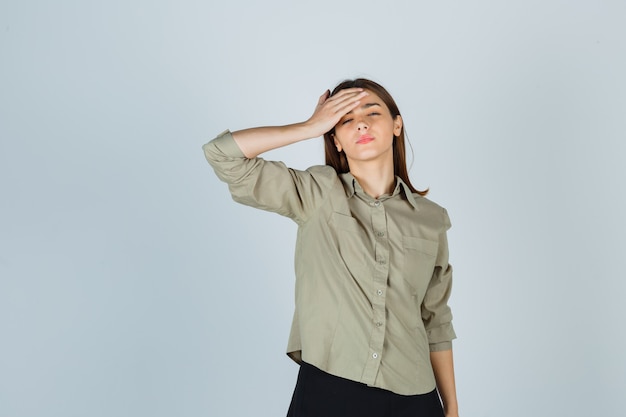 Young lady holding hand forehead in shirt, skirt and looking tired