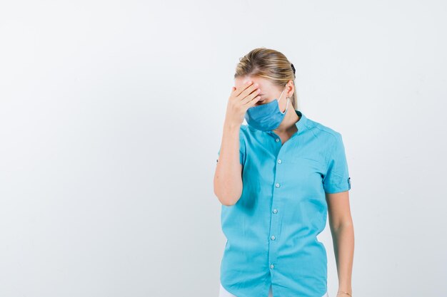 Young lady holding hand on forehead in t-shirt, mask and looking tired