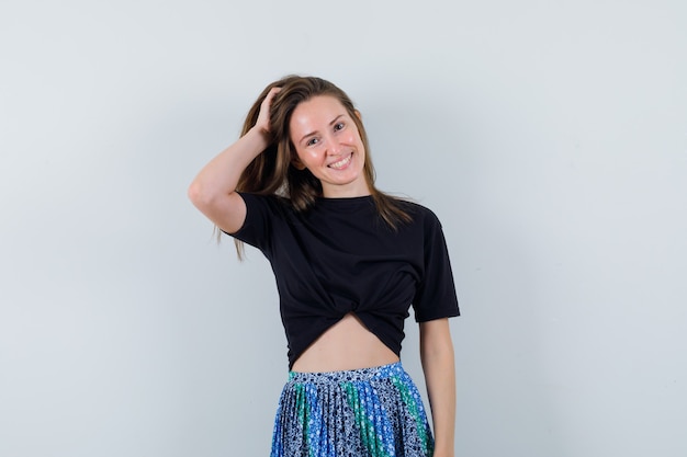 Young lady holding hand on head in blouse, skirt and looking alluring