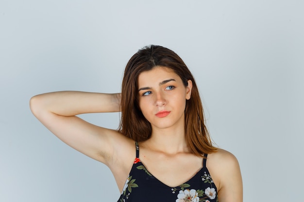 Young lady holding hand behind head in floral top and looking wistful