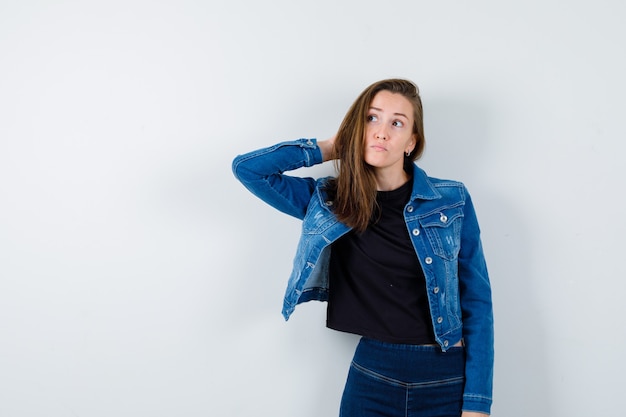 Young lady holding hand behind head and looking hesitant , front view.