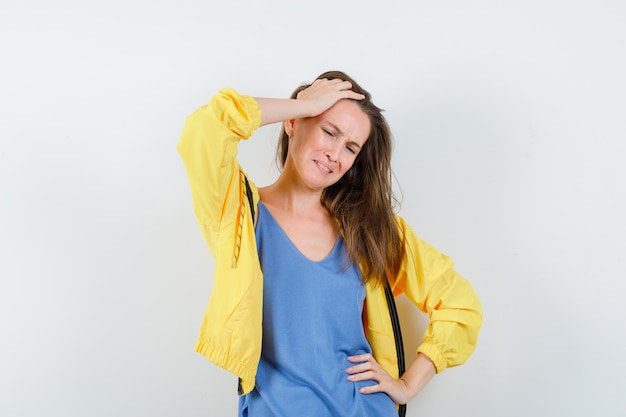 Young lady holding hand on head in t-shirt, jacket and looking mournful. front view.