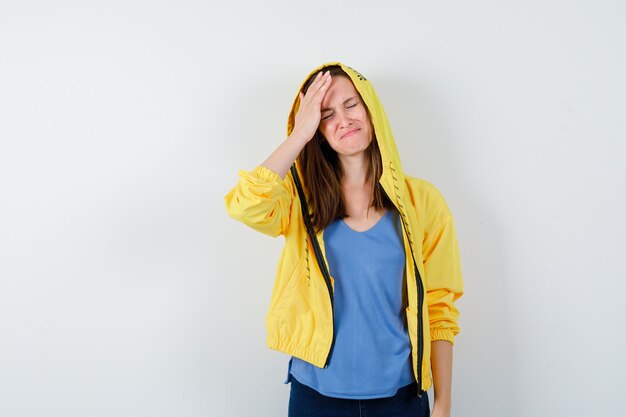 Молодая леди, держащая руку на голове в футболке, куртке и грустный вид, вид спереди.