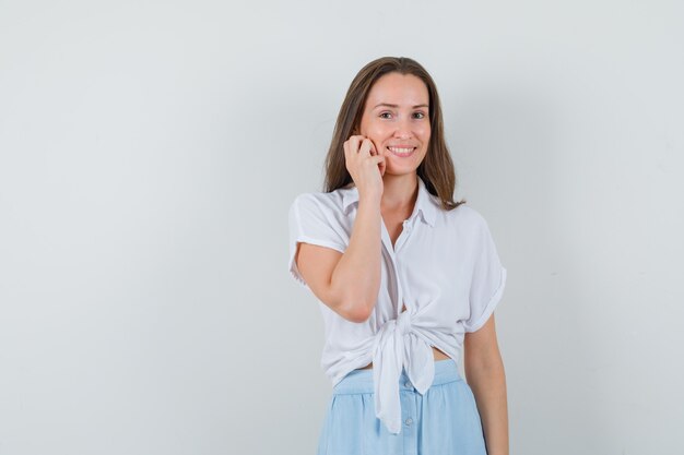 Young lady holding hand on her cheek while smiling in blouse and skirt and looking cute