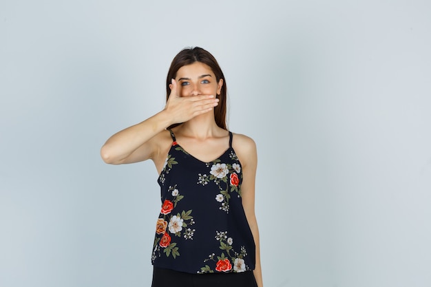 Young lady holding hand on mouth in blouse and looking positive , front view.