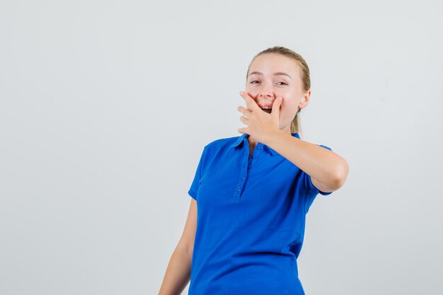 Young lady holding hand on mouth in blue t-shirt and looking happy