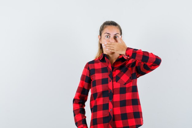 Free photo young lady holding hand on mouth in casual shirt and looking scared. front view.