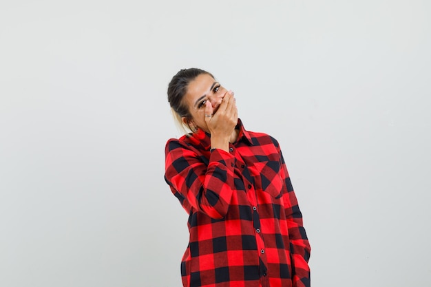 Free photo young lady holding hand on mouth in checked shirt and looking joyful