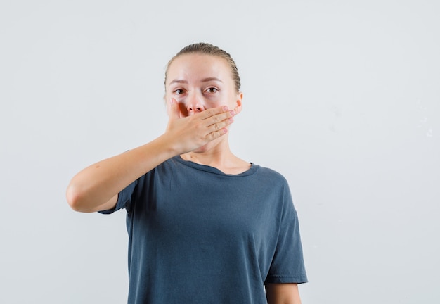 Young lady holding hand on mouth in grey t-shirt and looking surprised