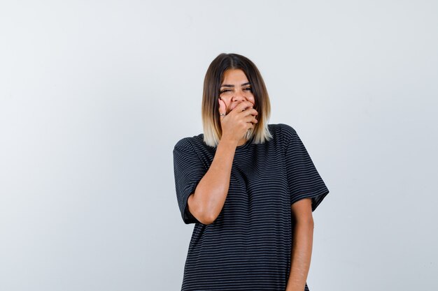 Young lady holding hand on mouth in polo dress and looking positive. front view.