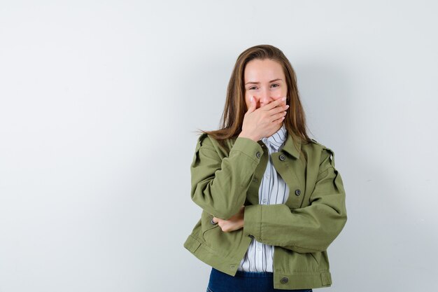 Young lady holding hand on mouth in shirt, jacket and looking merry. front view.