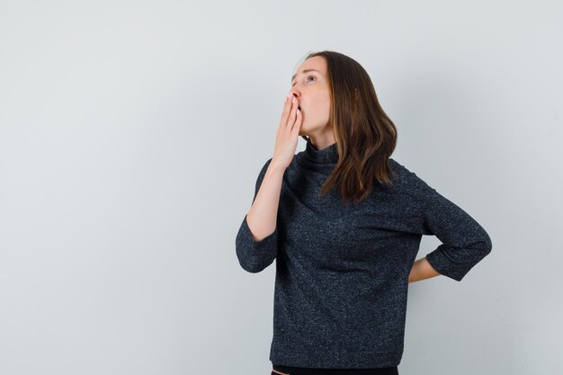 Young lady holding hand on mouth in shirt and looking thoughtful