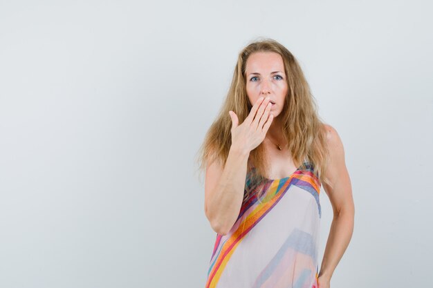 Young lady holding hand on mouth in summer dress and looking surprised. 