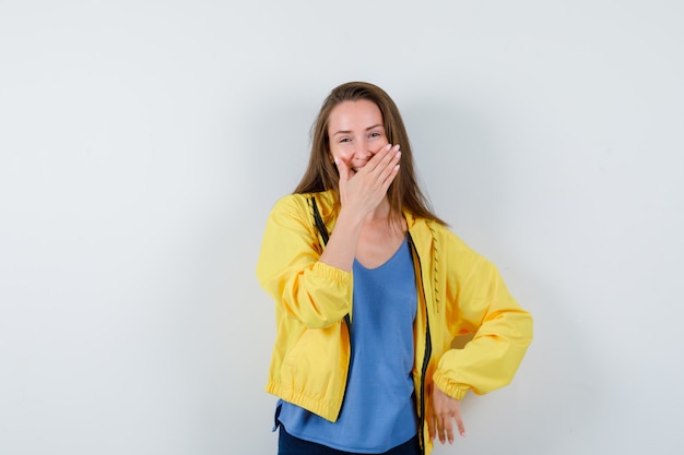 Young lady holding hand on mouth in t-shirt and looking glad , front view.