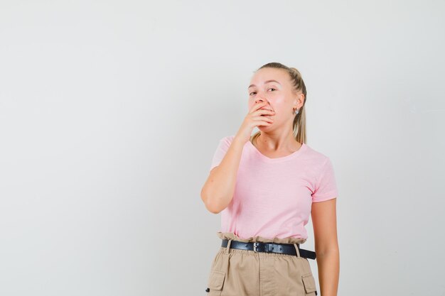 Young lady holding hand on mouth in t-shirts and pants and looking surprised