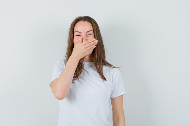 Young lady holding hand on mouth in white t-shirt and looking happy 