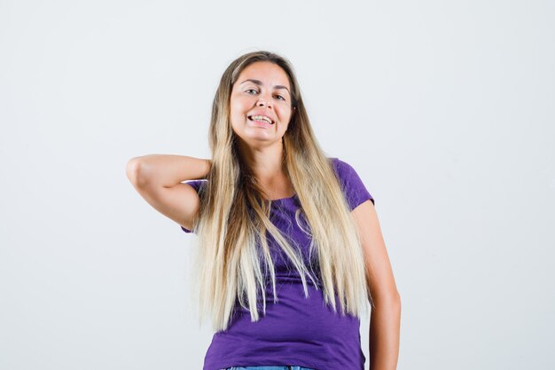 Young lady holding hand on neck in violet t-shirt and looking pretty. front view.