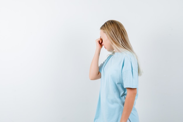 Young lady holding hand on nose in t-shirt and looking exhausted , front view.