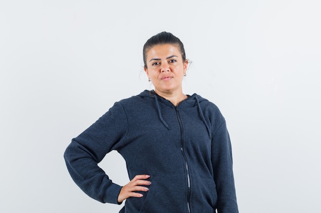 Young lady holding hand on waist in jacket and looking calm. front view.