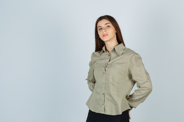 Young lady holding hands behind back in shirt, skirt and looking sensible , front view.