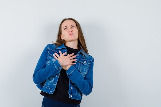 Free photo young lady holding hands on chest in blouse, jacket and looking gloomy, front view.