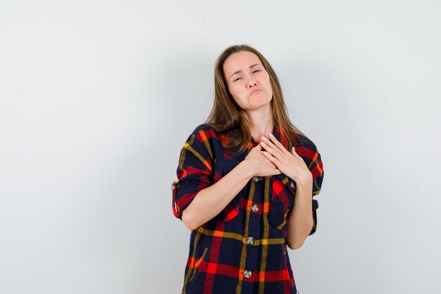 Young lady holding hands on chest in casual shirt and looking depressed. front view.