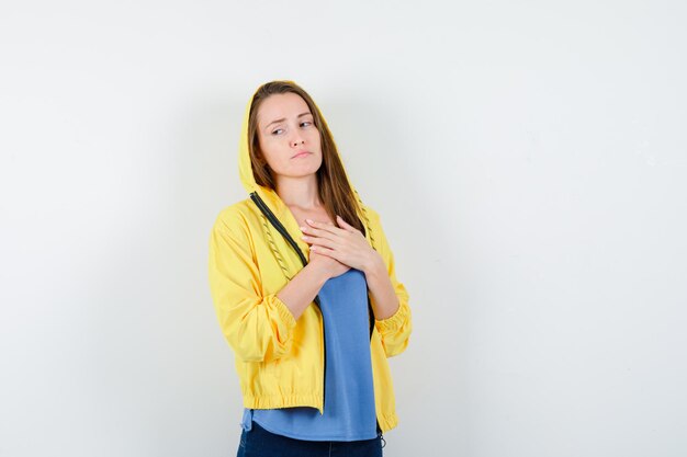 Девушка в футболке, куртке и задумчиво смотрит на грудь, держась за руки на груди