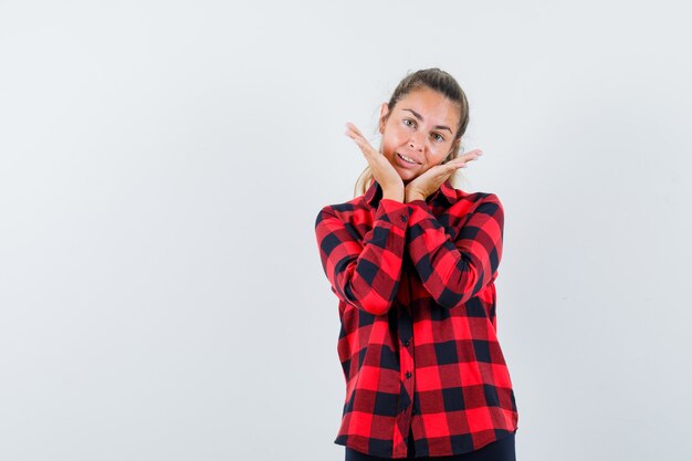 Young lady holding hands under chin in checked shirt and looking cute