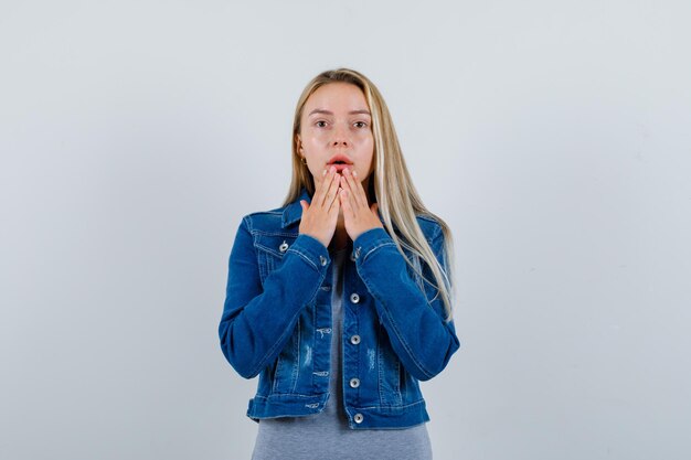 Young lady holding hands on chin in t-shirt, denim jacket, skirt and looking thoughtful.