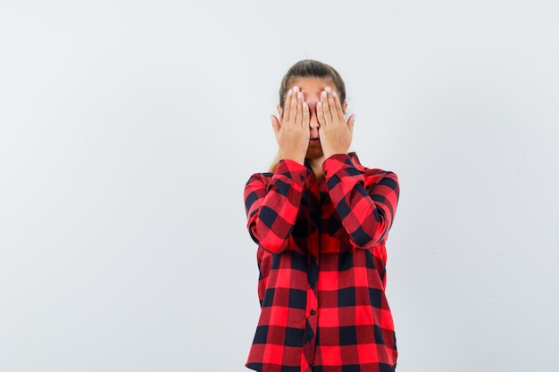 Free photo young lady holding hands on eyes in casual shirt and looking scared , front view.