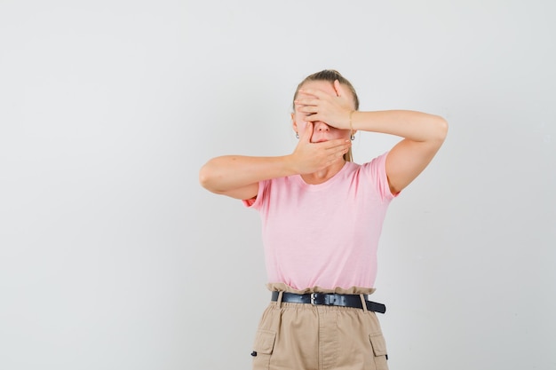 Young lady holding hands on eyes and mouth in t-shirts and pants and looking scared