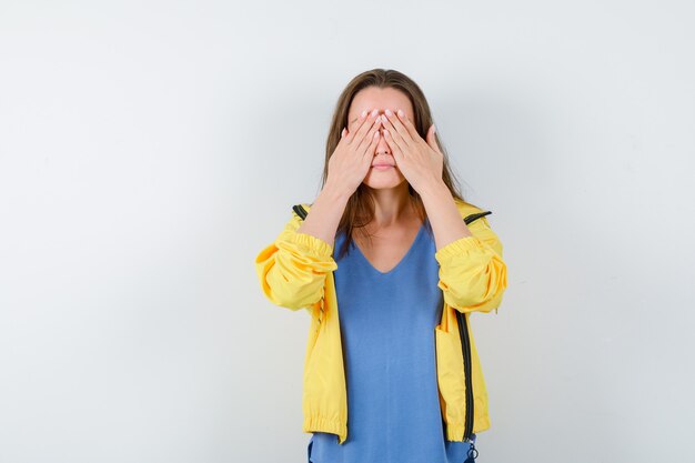 Young lady holding hands on eyes in t-shirt and looking calm , front view.