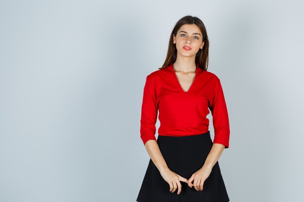 Young lady holding hands in front of her in red blouse, black skirt and looking pretty