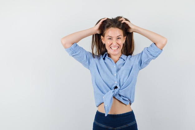 Giovane donna che tiene le mani nei capelli in camicia blu, pantaloni e sembra pazza.