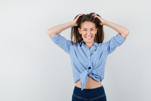 Young lady holding hands in hair in blue shirt, pants and looking crazy.