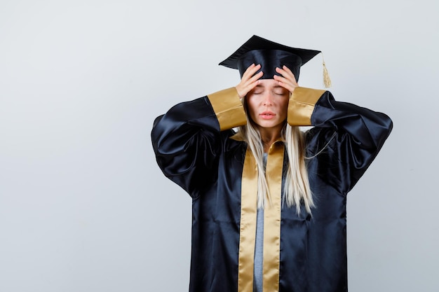 Free photo young lady holding hands on head in academic dress and looking fatigued