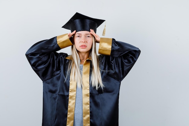 Foto gratuita giovane donna che si tiene per mano sulla testa in abito accademico e sembra affaticata.