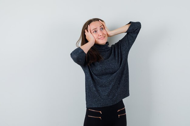 Young lady holding hands on head in casual shirt and looking happy. front view.