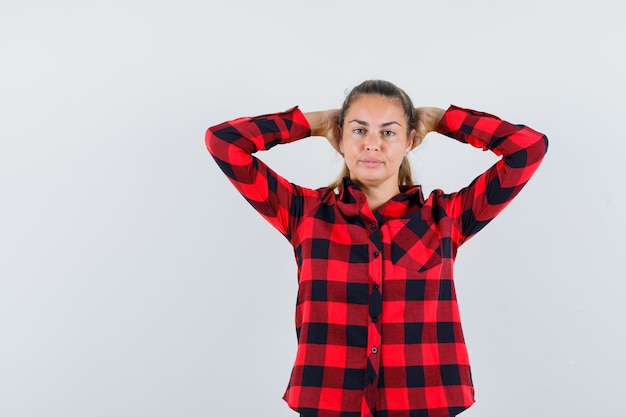 Free photo young lady holding hands behind head in checked shirt and looking pretty