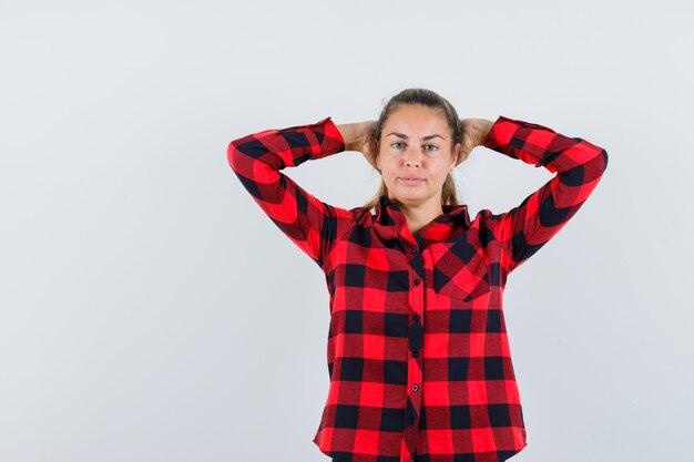 Young lady holding hands behind head in checked shirt and looking pretty