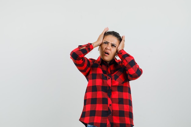 Young lady holding hands to head in checked shirt and looking regretful