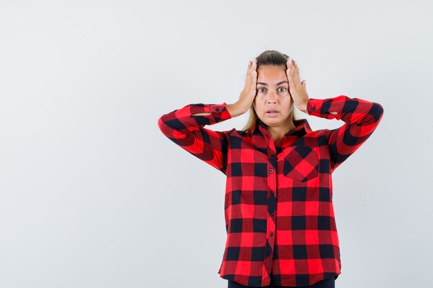 Young lady holding hands on head in checked shirt and looking wistful