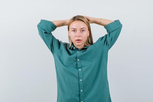 Foto gratuita giovane donna che si tiene per mano dietro la testa in camicia verde e sembra sicura