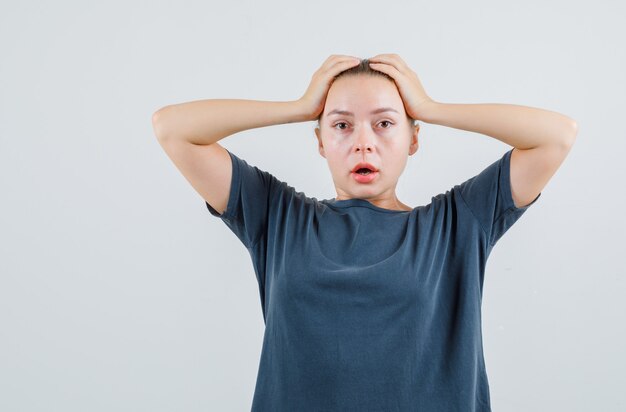 Young lady holding hands on head in grey t-shirt and looking confused