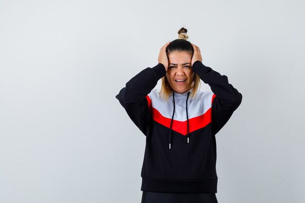 Young lady holding hands on head in hoodie sweater and looking cheery.