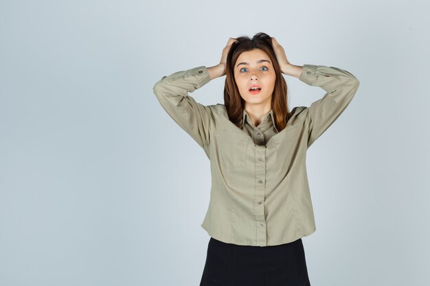 Free photo young lady holding hands on head in shirt, skirt and looking bewildered , front view.